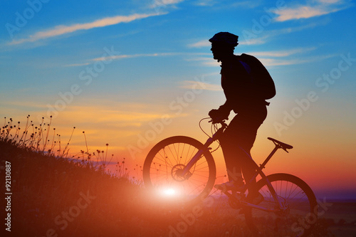 Silhouette of a biker and bicycle on sunset background. © Aleksey