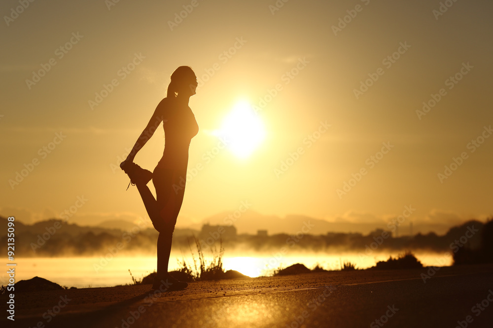 Silhouette of a fitness woman stretching at sunrise - obrazy, fototapety, plakaty 