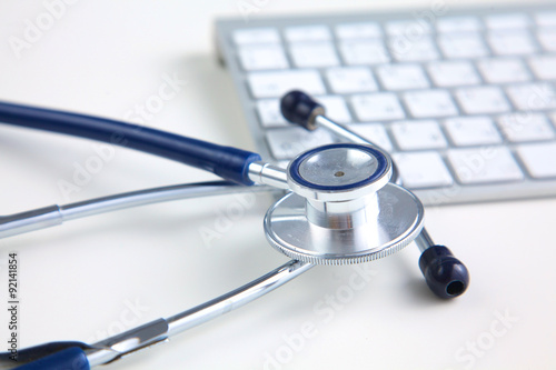A medical stethoscope near a laptop on a wooden table, on white