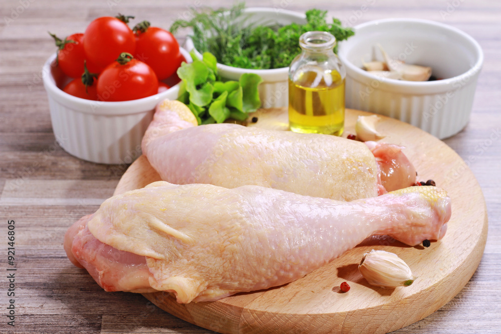 Raw chicken legs decorated with salad, olive oil and cherry tomatoes on white plate. Diet food, healthy lifestyle Raw chicken legs decorated with salad, olive oil and cherry tomatoes on white plate. Diet food, healthy lifestyle