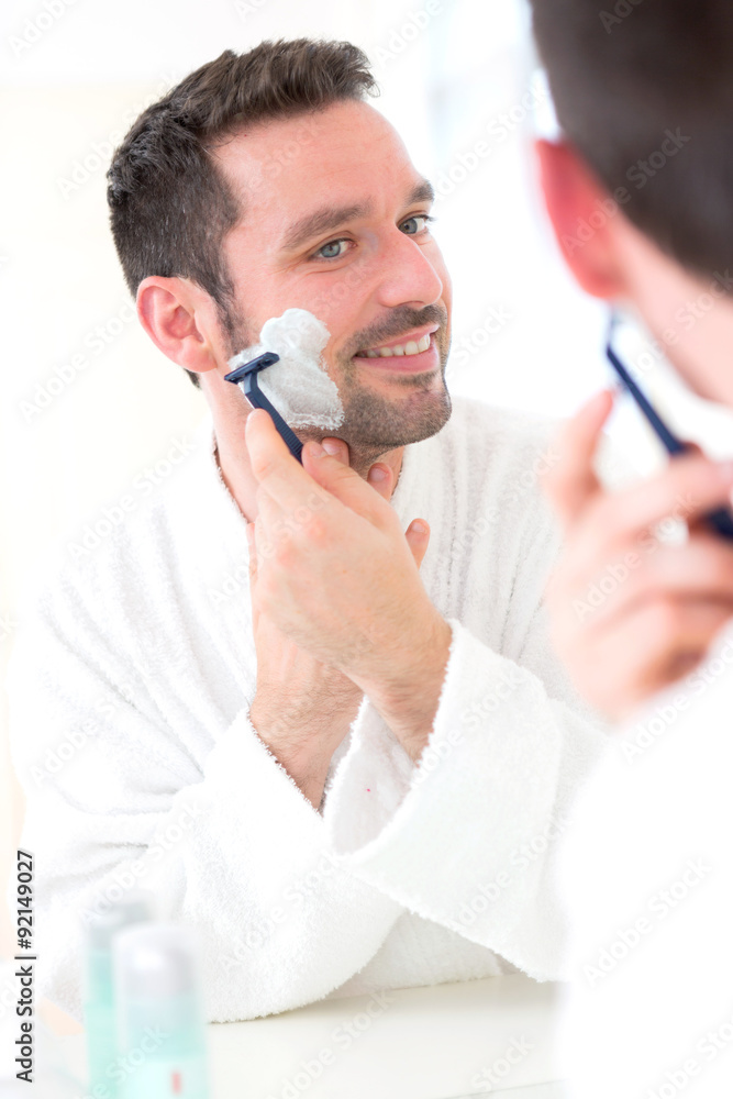 Young attractive man shaving his beard in front of a mirror
