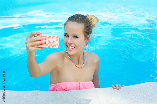 Trendy young woman posing on her phone camera and taking a photo of herself in the pool