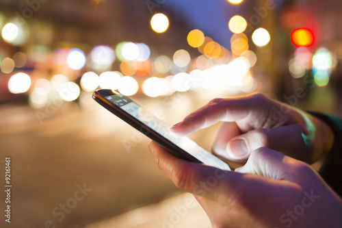 Man using his Mobile Phone in the street, night light bokeh Background photo