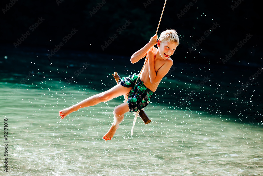7 years boy having fun on rope swing above river. Stock Photo