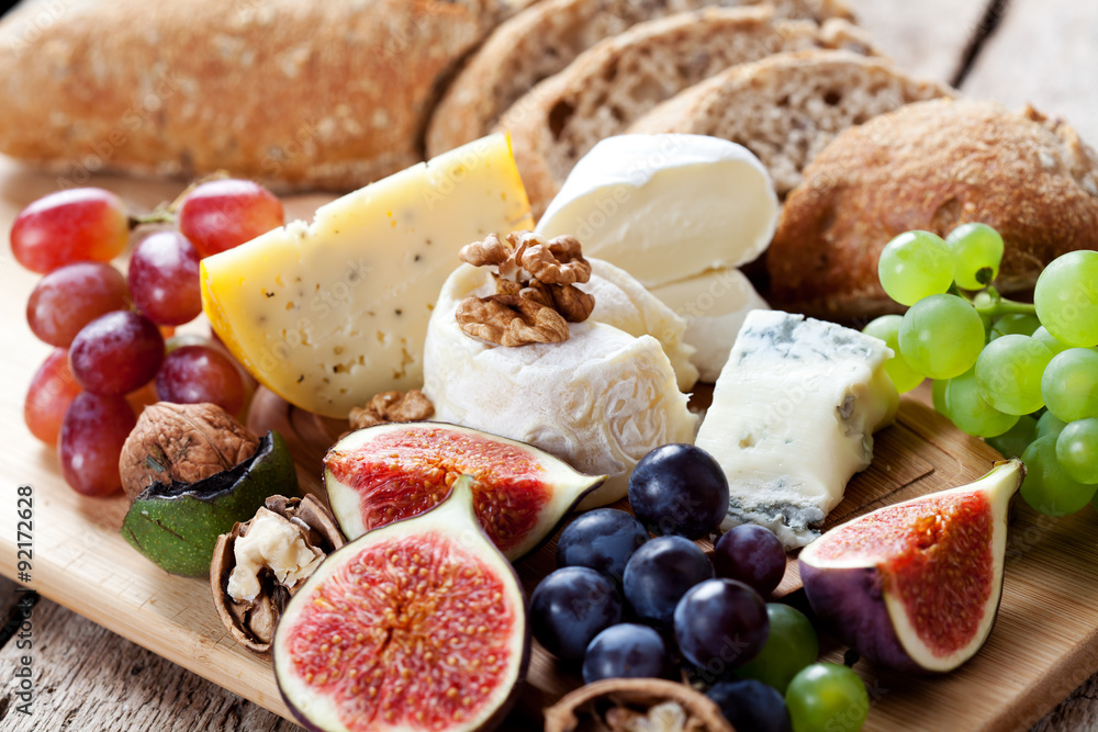 Cheese platter: variety of cheeses on wooden plate with fruits and bread
