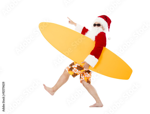 Canvas Print Happy Santa Claus holding surf board with pointing gesture