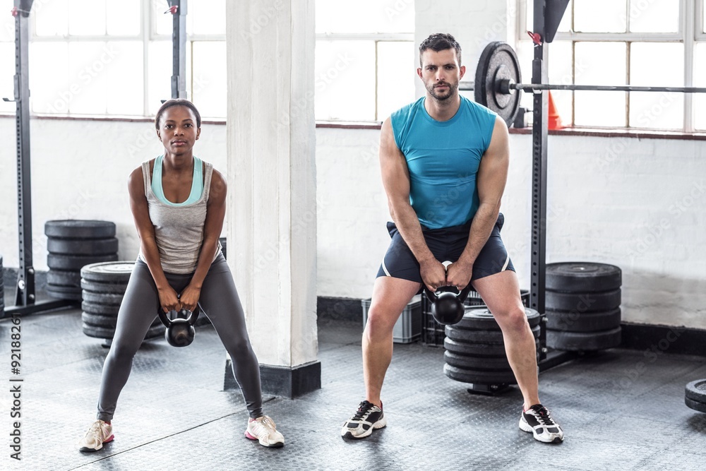 A muscular couple lifting kettlebells A muscular couple lifting kettlebells