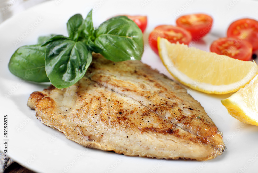 Dish of fish fillet with basil and lemon on plate close up Dish of fish fillet with basil and lemon on plate close up