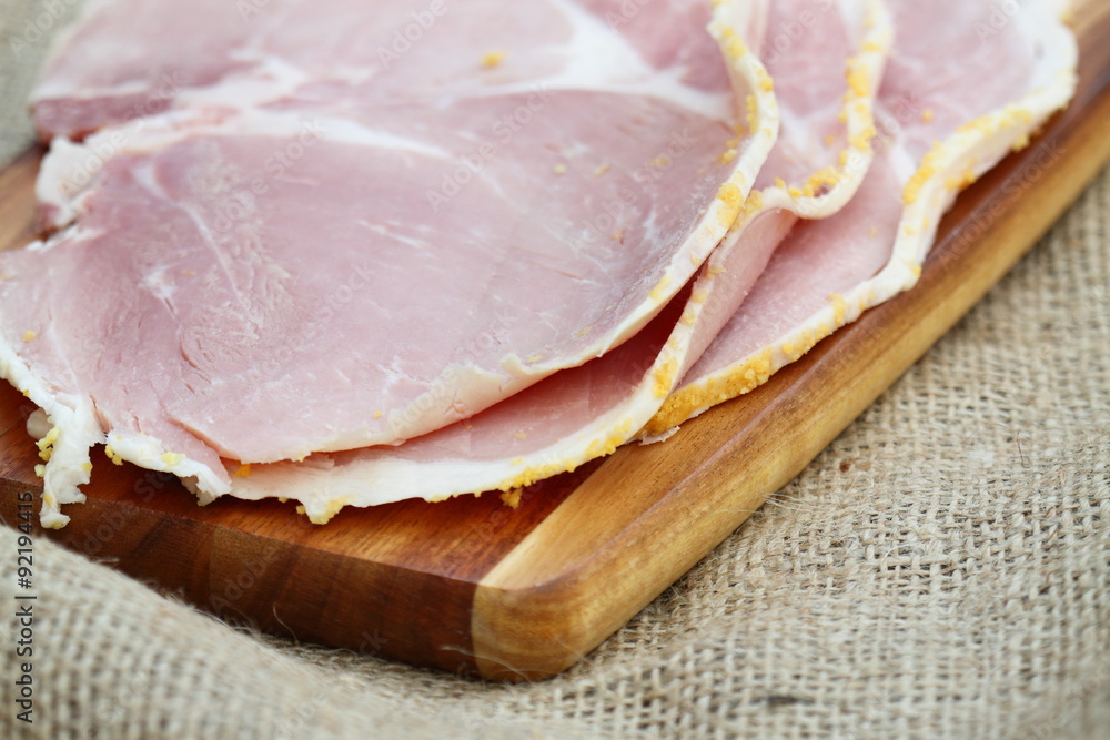 Ham slices wooden chopping board hessian.
Slices of boiled ham on a wooden chopping board.