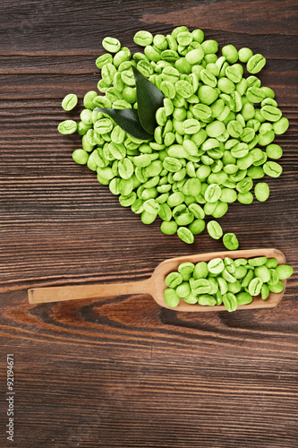 Green coffee beans with leaves and spoon on wooden table close up