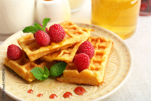 Sweet homemade waffles with fresh raspberries on plate, on light background
