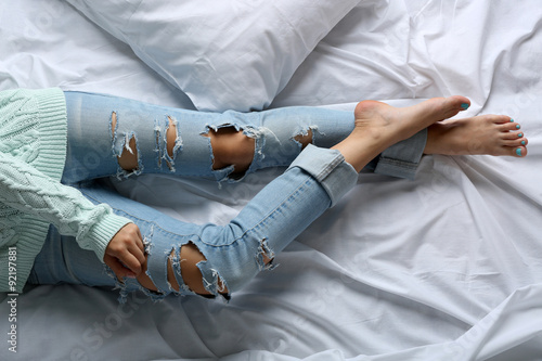 Woman in blue jeans on bed top view