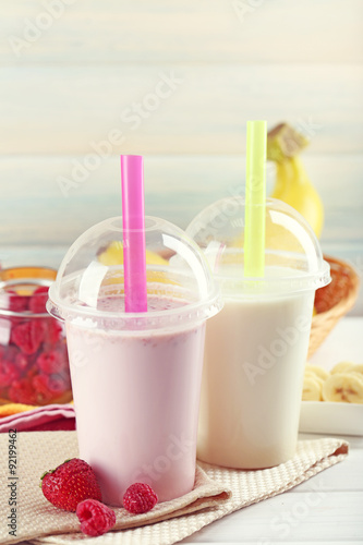 Plastic cup of milkshake on light wooden background