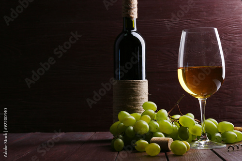 Bottle and glass of wine with grape on wooden background