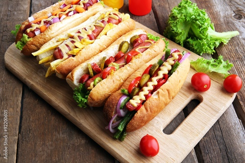 Fresh hot dogs on cutting board and bottles on wooden background