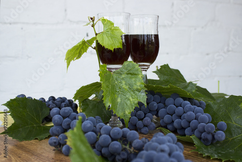 Red wine in stemware standing on the wooden background with grapes and green leaves