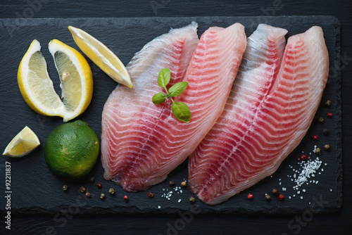 Raw tilapia with seasonings on a stone slate dish, above view