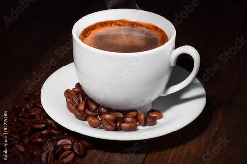 White coffee cup and coffee beans on a wooden table. Dark background.