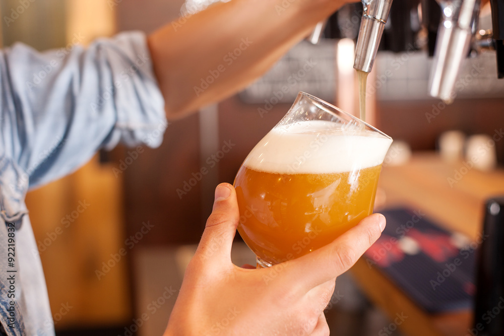 Cheerful young bartender is pouring lager in pub Cheerful young bartender is pouring lager in pub