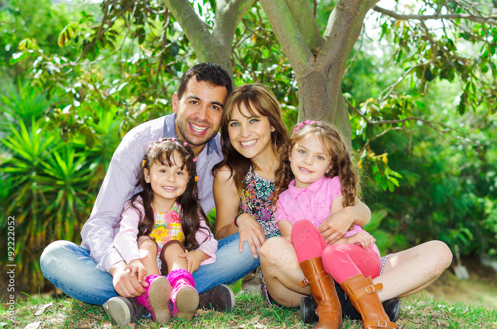 Fototapeta premium Beautiful hispanic family of four sitting outside on grass