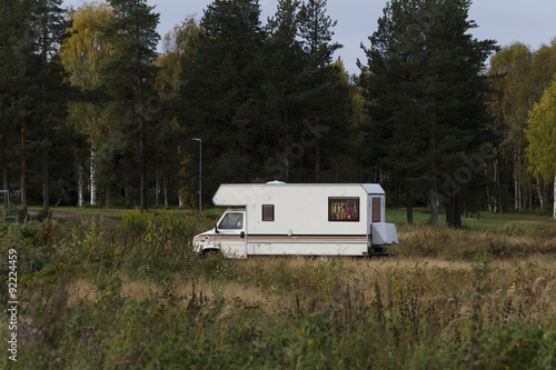 A parked camper on a field with some trees in the background