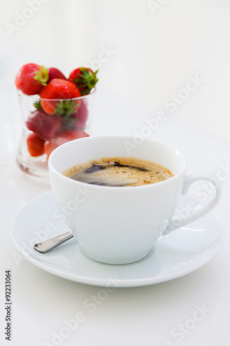 A cup of black coffee and strawberries on a white table