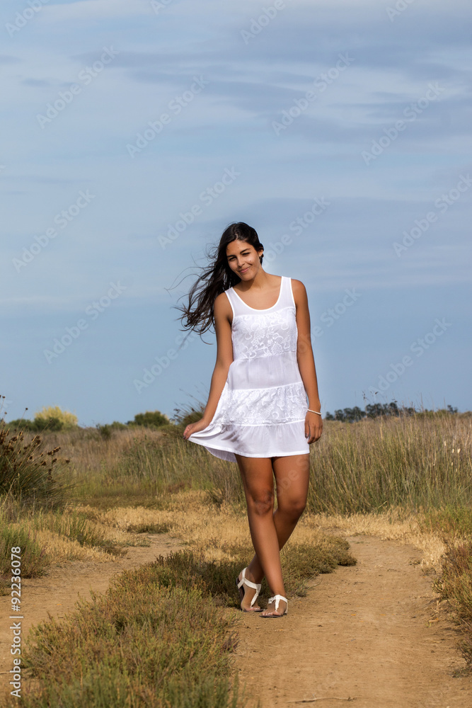 Close view of a beautiful woman on a white dress, walking on a dirt path.