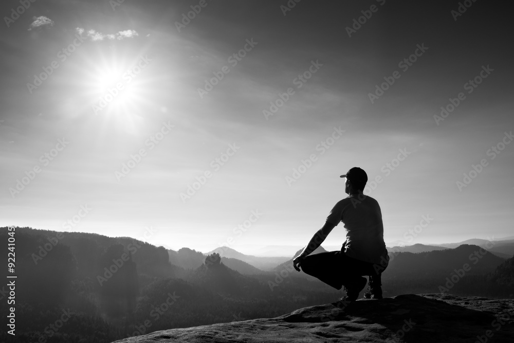 Runner in red cap and  in dark sportswear. Man sit  in squatting position on a rock in heather bushes, enjoy autumn scenery