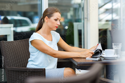 Attractive young woman reads a newspaper sitting in a cafe