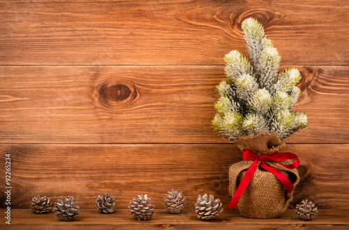 Artificial little christmas tree in pot with cones on the wooden background.