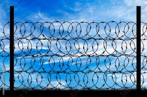 Silhouette of a metal fence with barbed wire