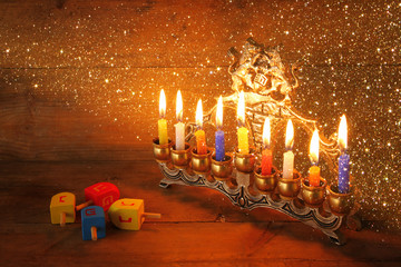 low key image of jewish holiday Hanukkah with menorah (traditional Candelabra) and wooden dreidels spinning top over chalkboard background, room for text
