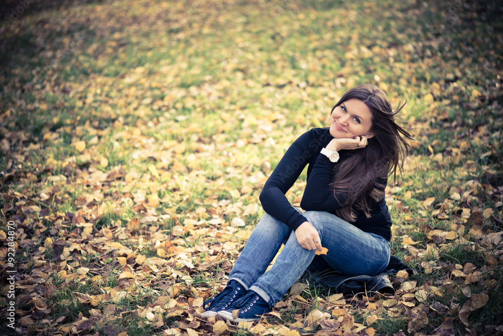 young woman sits on leaves in autumn park young woman sits on leaves in autumn park