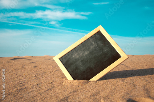 closeup of a chalkboard with a wooden frame, placed on the sand of a beach