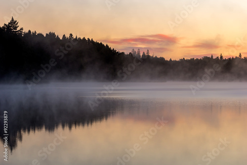 Fototapeta Naklejka Na Ścianę i Meble -  View over lake befoer the sun rises, with vivid colors in the sky and mist on the water