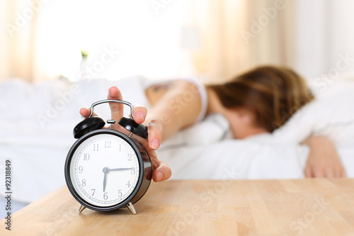 Sleepy young woman trying kill alarm clock photo