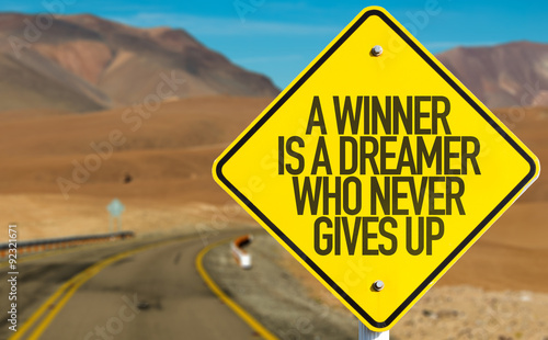 A Winner Is A Dreamer Who Never Gives Up sign on desert road