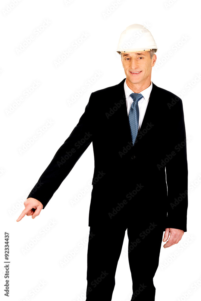 Smiling businessman with hard hat pointing down Smiling businessman with hard hat pointing down