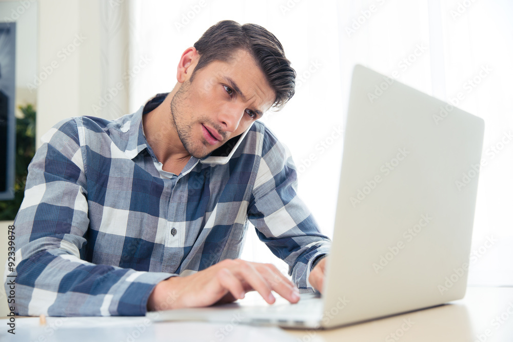 Man paying his bills with laptop while talking on phone Man paying his bills with laptop while talking on phone