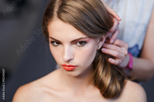 Young blonde girl applying make-up by make-up artist.