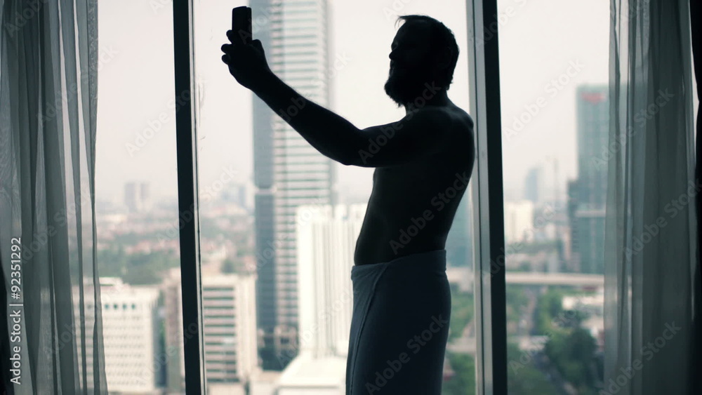 Young man in towel taking selfie photo with cellphone by window
Young man in towel taking selfie photo with cellphone by window