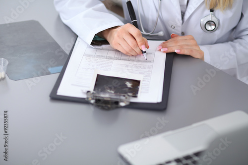 Close up of female doctor filling up a medical history form, sitting at the table in hospital