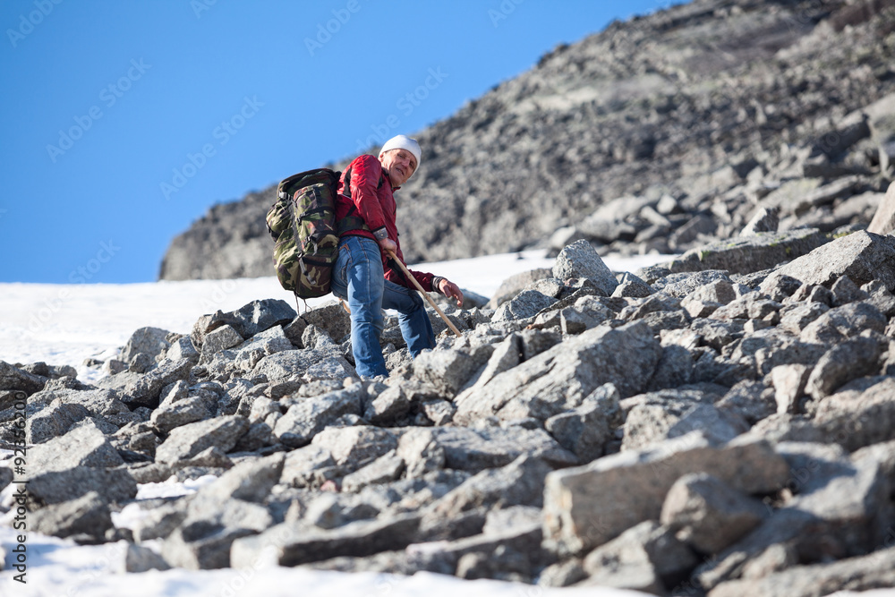Senior Caucasian hiker climbing alone in steep slope mountains at summer season