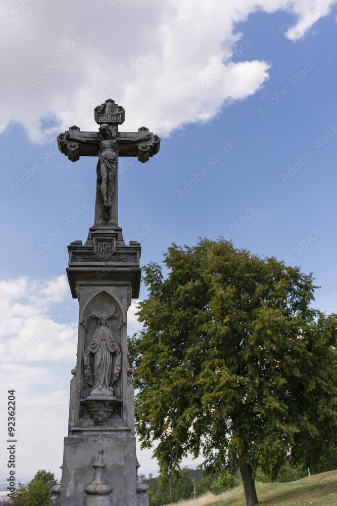 stone cross with Jesus and tree in the background