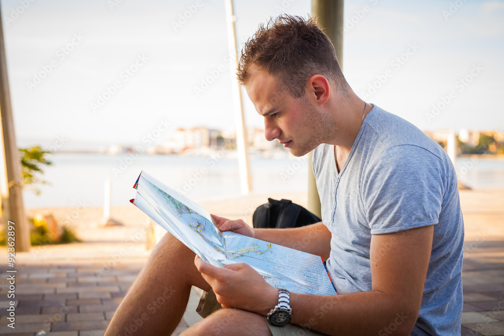 Young tourist sitting under palm tree and looking at the map. Positive emotions.