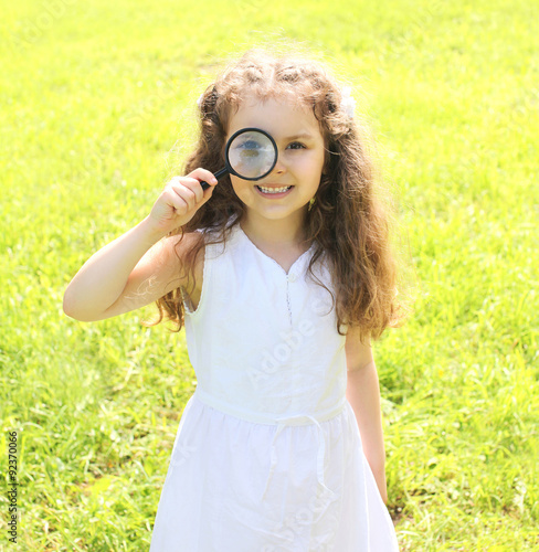 Little girl child looking through a magnifying glass on nature s