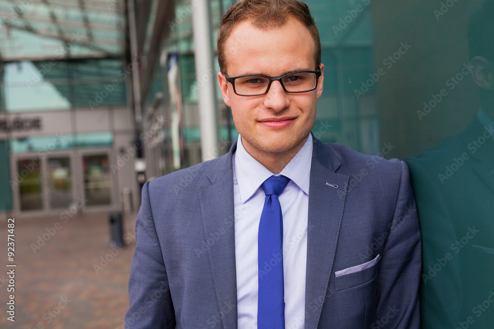 Portrait of young businessman standing in front of office block. Portrait of young businessman standing in front of office block.