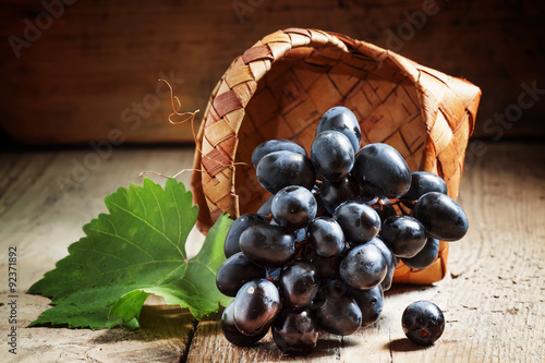 Dark grapes in birch wicker basket on an old wooden table, selec photo