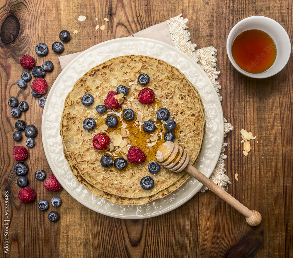delicious pancakes with fresh berries with honey, almonds cup of tea with honey spoon on white plate with napkin on wooden rustic background top view delicious pancakes with fresh berries with honey, almonds cup of tea with honey spoon on white plate with napkin on wooden rustic background top view