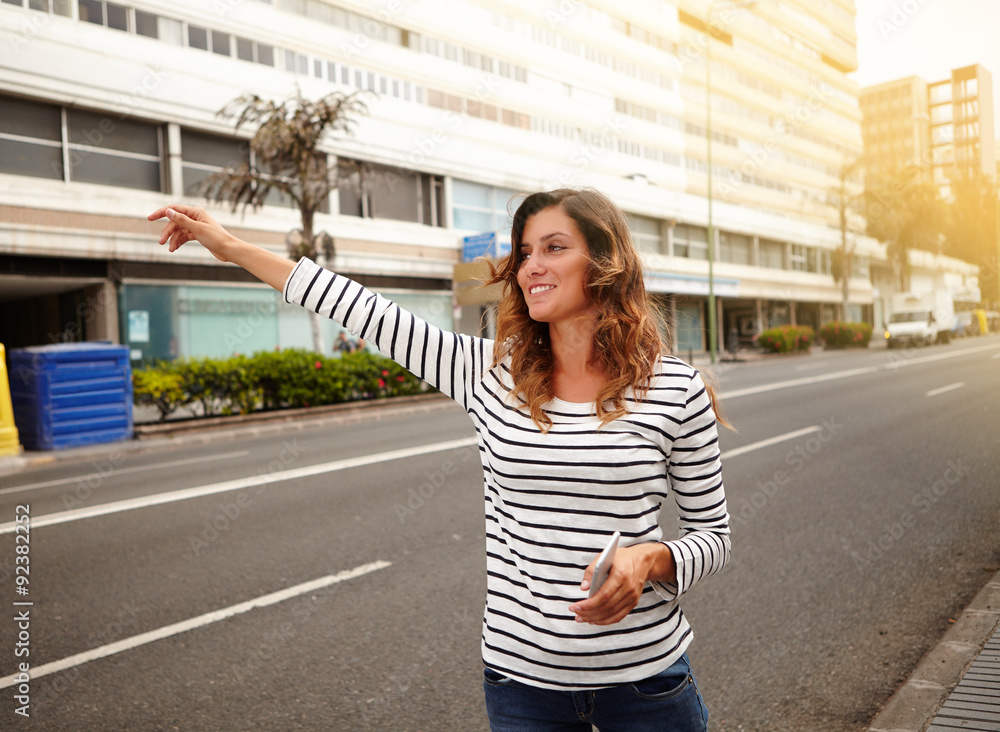 Cheerful young woman hailing a cab on city street